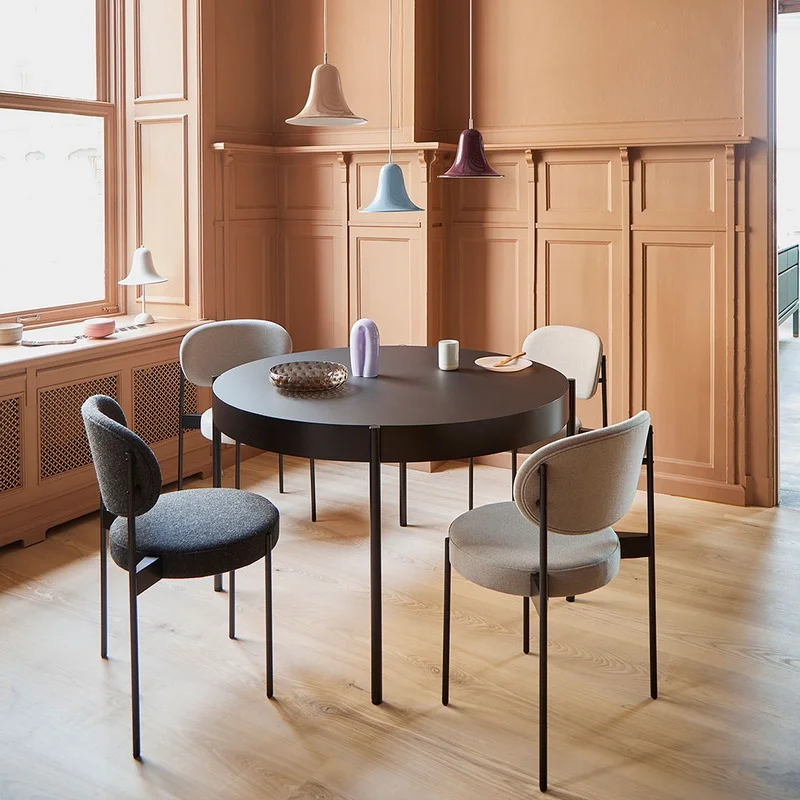 Round black dining table with six upholstered chairs in a peach-toned paneled room with pendant lights above.](https://)