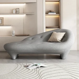 Modern grey textured Chaise Longue Sofa Slipper Chair with a cream pillow in a minimalist room with built-in lit shelving.