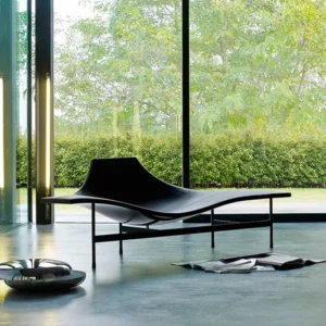 Sleek black Terminal 1 Chaise Accent with a curved, ergonomic design set against a floor-to-ceiling window view of lush greenery.