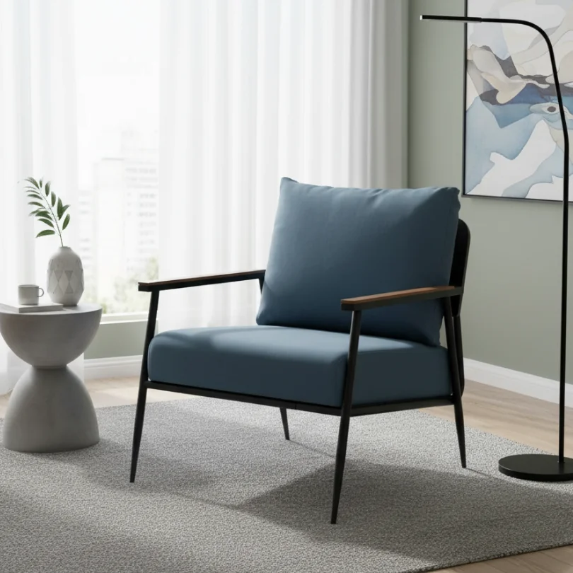 Blue upholstered armchair with wooden arms in a bright, modern living room beside a round side table with a vase and mug.