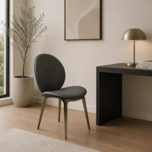 Dark gray upholstered chair with brass legs beside a black desk and gold lamp in a bright, minimalist home office corner.