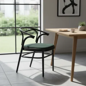 Modern black chair with curved arms and a green cushioned seat beside a light wooden table in a sunlit dining area.