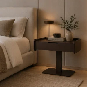 Bedside nightstand with a drawer, warm lamp, Kinfolk book, candle, and a ceramic vase with greenery.
