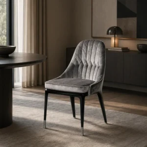 Gray tufted dining chair with black legs set beside a round dark table in a modern, muted living/dining space.