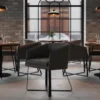 Modern restaurant interior with gray armchairs, wooden tables, brick walls, and a large grid window.
