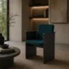 Teal upholstered armchair with a black metal frame in a modern living room, beside a round coffee table and plant.