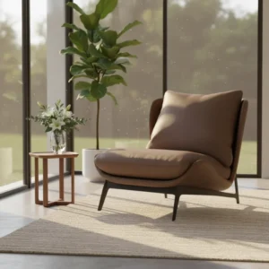 Brown leather lounge chair with a curved back and black legs, by large windows next to a small wooden side table with flowers in a vase on it.