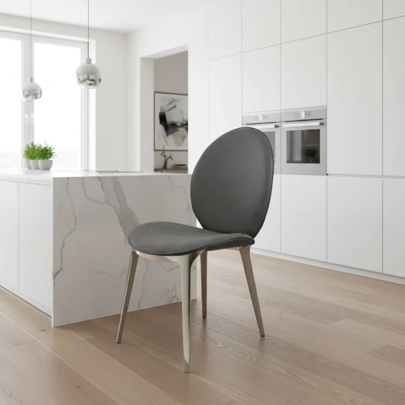 Modern white kitchen with a marble island, gray chair in the foreground, and built-in ovens along white cabinetry.