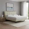 Queen bed with tufted beige headboard in a modern bedroom, flanked by wooden nightstands and a white lamp, near a large window with sheer curtains