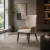 Beige high-back upholstered armchair with dark legs in a modern living room by a large window.