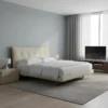 Contemporary bedroom with a cream upholstered bed, white bedding, and matching nightstands on a gray rug. a TV sits on a wooden console by the window.