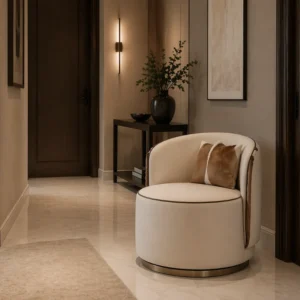 Cream circular lounge chair with brown cushions sits in a beige-toned hallway, next to a console table with a black vase and greenery.