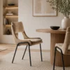 Round wooden dining table with a ribbed pedestal base, beige upholstered chairs, and a tall vase with greenery in a minimalist dining room setting.