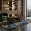 Modern living room with a tall wooden bookshelf, green velvet armchair, dark wood coffee table, blue and gold rug, and a floor lamp by a large window overlooking the cityscape.