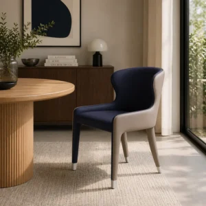 A modern dining nook with a round wood table, two-toned chair, and a cabinet against a neutral wall near a large window.