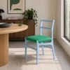 Blue chair with a green cushion placed beside a round wooden table in a bright, modern dining space with a plant and cabinet in the background.