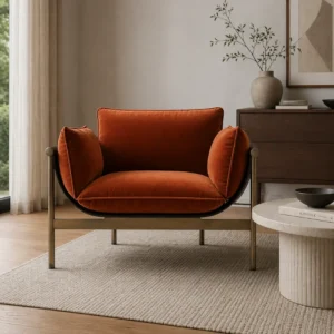 Orange velvet lounge chair with a black metal frame sits in a modern living room on a beige rug, with a round coffee table and wooden dresser nearby.