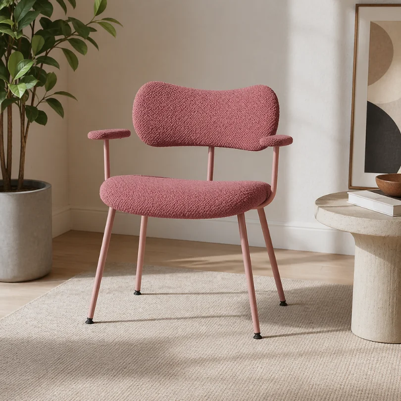Pink textured upholstered lounge chair with curved back and slim legs in a bright living room beside a potted plant and a round side table.