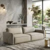 Beige modular sofa with quilted arms in a marble-walled living room, overlooking a landscaped garden.