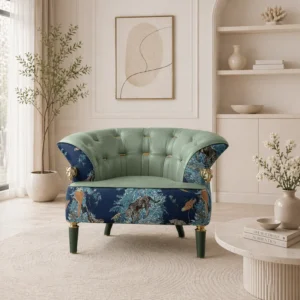 Tufted emerald green velvet chair with a blue botanical-printed base, gold accents, and dark green legs in a bright beige living room with plants and abstract art above.