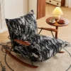 Black-and-white patterned rocking chair with wooden arms beside a round side table holding a lamp, tea cup, and a plate of strawberries on a beige rug.