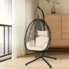 Black hanging egg chair with cream cushions, in a bright room beside a window.