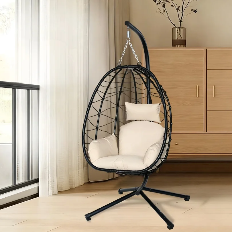 Black hanging egg chair with cream cushions, in a bright room beside a window.