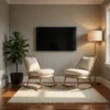 Cozy living room corner with two cream upholstered rocking chairs facing a wall-mounted flat-screen TV, a tall floor lamp, and a green potted plant on a wooden floor with a white rug.
