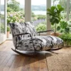 Rocking chair with black-and-white upholstery in a sunlit greenhouse-style room surrounded by potted plants and a garden view outside.