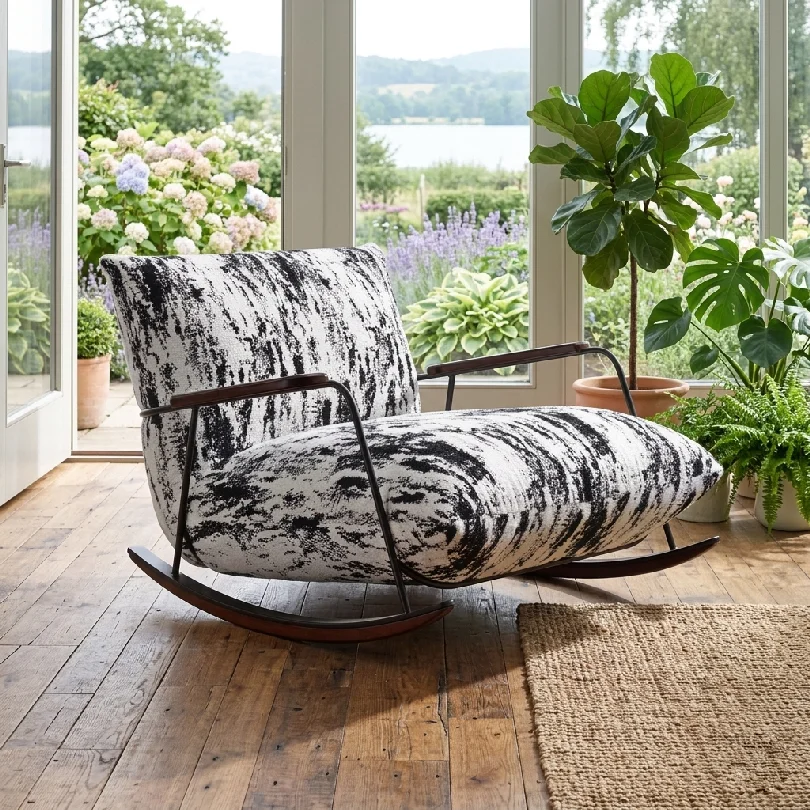 Rocking chair with black-and-white upholstery in a sunlit greenhouse-style room surrounded by potted plants and a garden view outside.