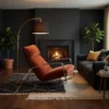 Cozy living room with an orange recliner, brass arc floor lamp, and a glowing fireplace, set against dark walls with potted plants and a gray sofa.