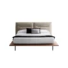 Modern platform bed with beige upholstered headboard, white bedding, and two accent pillows (black and gray). The low wooden frame and slim legs are visible beneath the mattress.