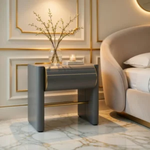 Luxurious bedroom scene with a modern gray nightstand, a glass vase with branches, a lit candle, and books beside a plush bed.