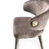 Grey velvet upholstered armchair with a curved back and a gold button accent, shown from the side against a white background.