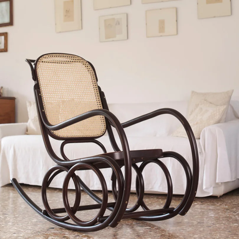 Wooden rocking chair with a caned back and seat in a light-filled living room next to a white sofa.