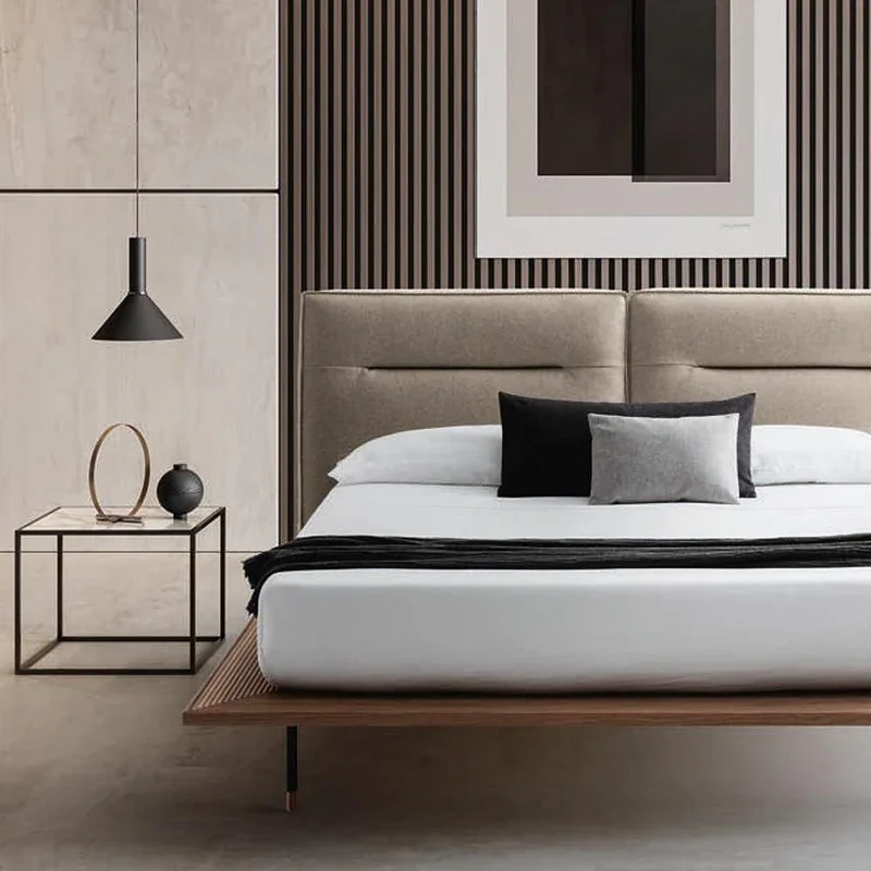 Modern bedroom with low platform bed, beige upholstered headboard, and white bedding with black and gray cushions.