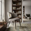 Gray upholstered chair with brass accent in a sunlit living room, a tall wooden bookcase behind, and a fireplace in the background.