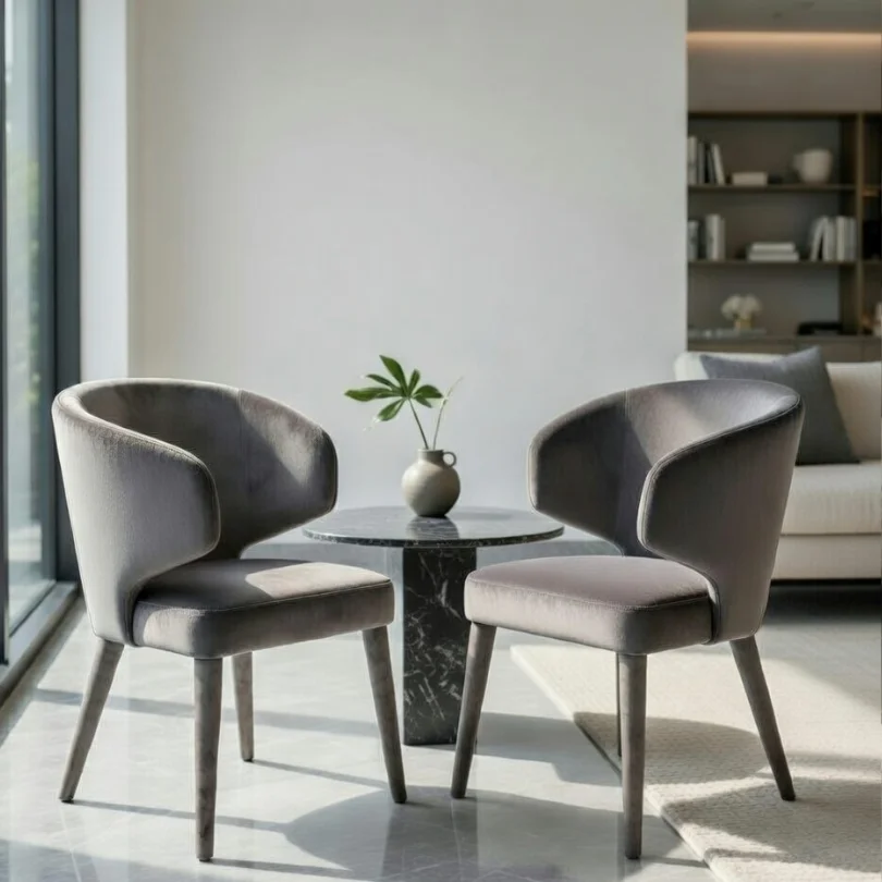 Two gray upholstered lounge chairs face a small round marble table with a vase and leaf in a bright, modern living room.