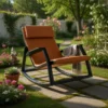 Orange cushioned lounge chair on a stone path in a sunny garden, with a gray blanket draped over the arm.