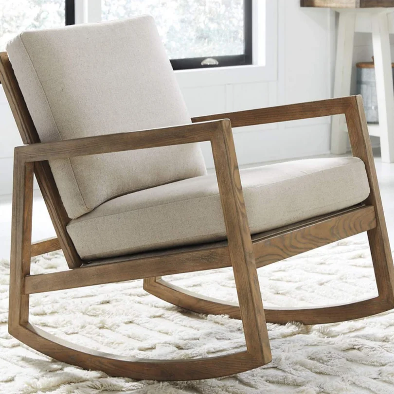 Wooden rocking chair with beige cushions on a fluffy white rug in a bright living room