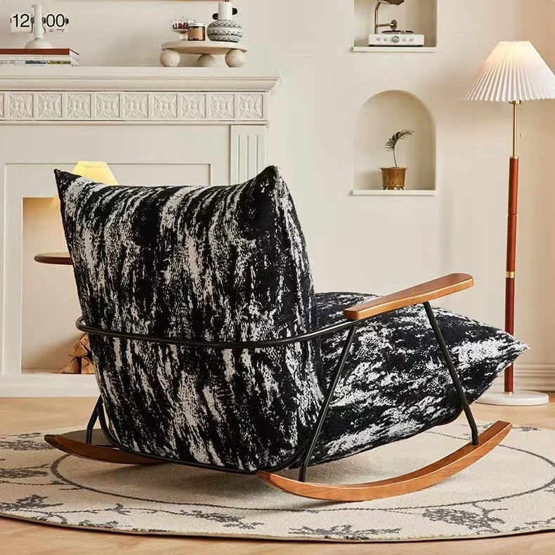 Modern rocking chair with black-and-white textured upholstery and wooden rockers in a cozy living room with a fireplace beside it.
