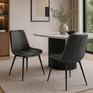 Modern dining area with two black upholstered chairs around a light marble table with a ribbed pedestal base on a beige rug.