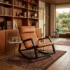 Contemporary tan leather lounge chair with dark wooden frame in a wood-furnished library with bookshelves and a rug.