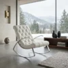 White tufted lounge chair with chrome legs in a bright living room, overlooking snowy mountains through large windows.