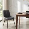Black upholstered dining chair with slender legs beside a wooden table set with plates and glassware in a bright marble-walled dining area.