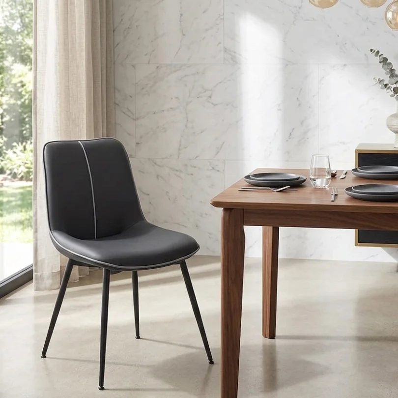 Black upholstered dining chair with slender legs beside a wooden table set with plates and glassware in a bright marble-walled dining area.