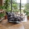 Rocking chair with a black-and-white patterned cushion in a sunlit plant-filled conservatory with large windows overlooking a garden and pond outside.