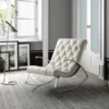 White tufted lounge chair with chrome legs in a bright, stylish living room near framed art and a brass floor lamp by a large window.