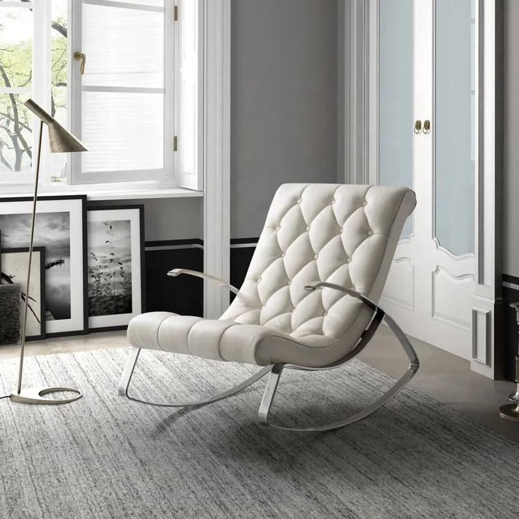 White tufted lounge chair with chrome legs in a bright, stylish living room near framed art and a brass floor lamp by a large window.