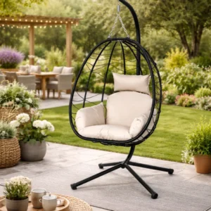 Outdoor hanging egg chair with beige cushions on a black stand in a garden patio setting.